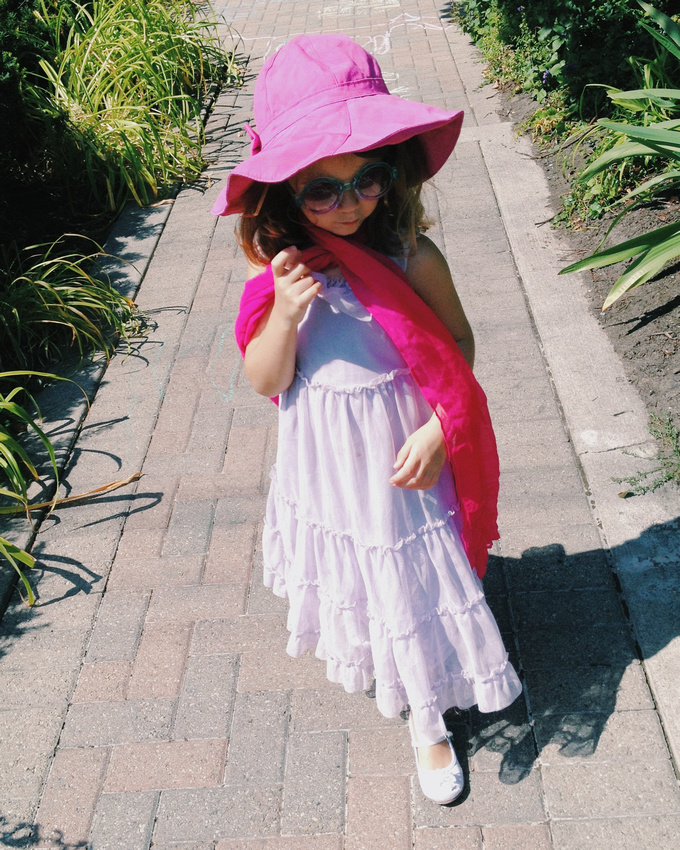 Girl wearing pink hat, a scarf, John Lennon sunglasses, and a fancy dress.