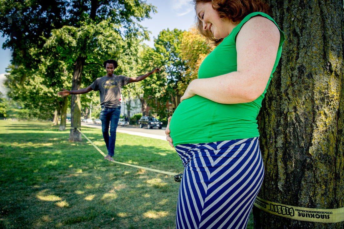 Pregnant woman leaning against tree, watching man on slackline