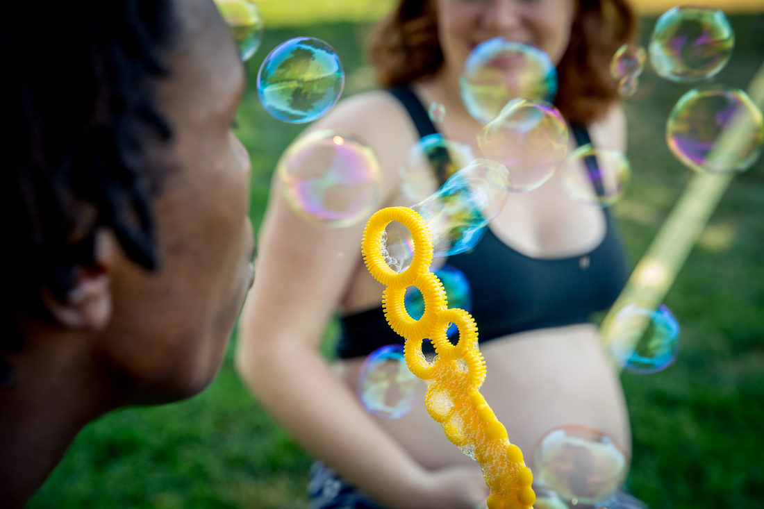 Man blowing bubbles at mother-to-be sitting on slackline